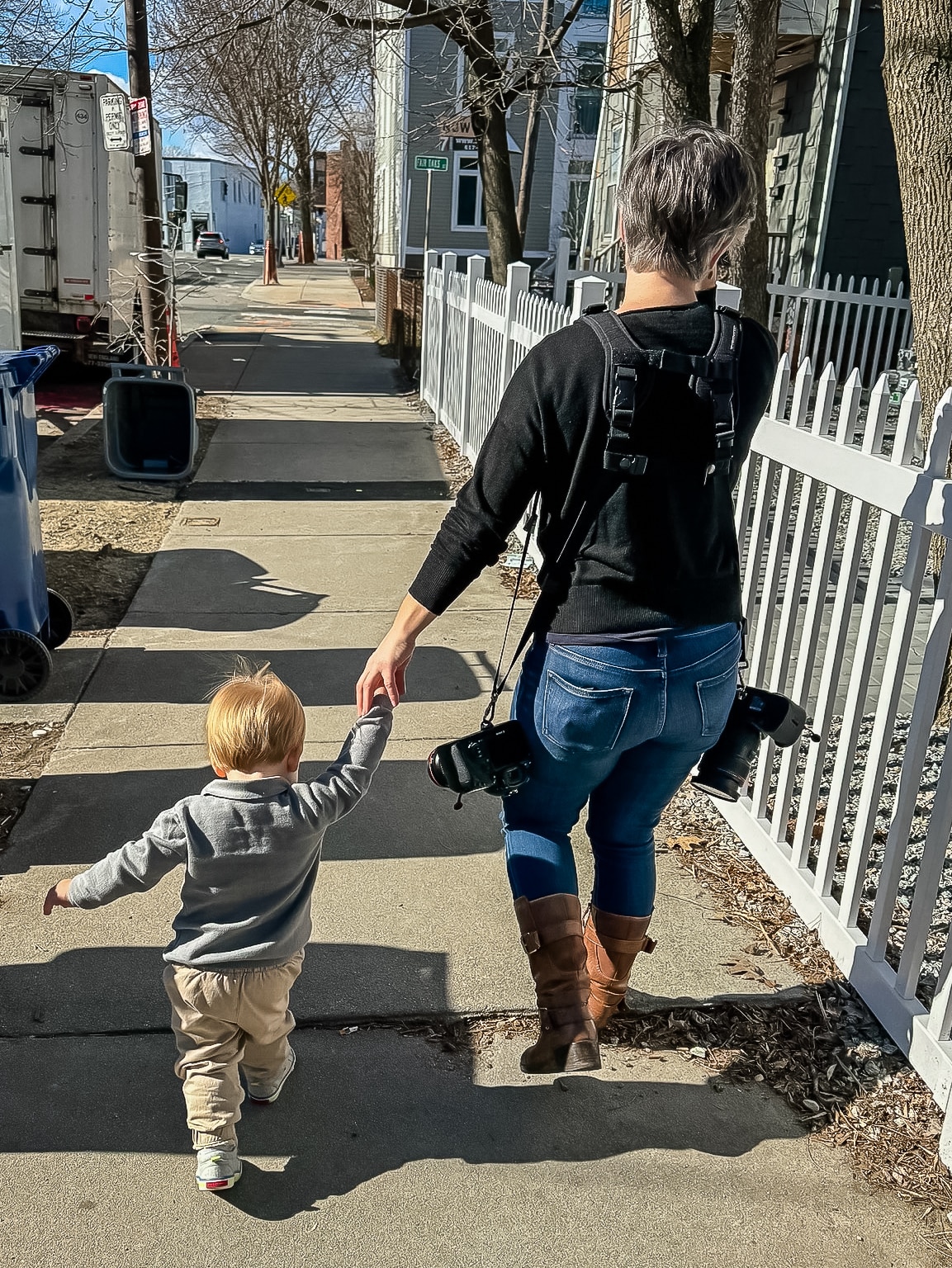 Photographer Emily Sterne walks on a sidewalk holding hands with one of her subjects, aged 2