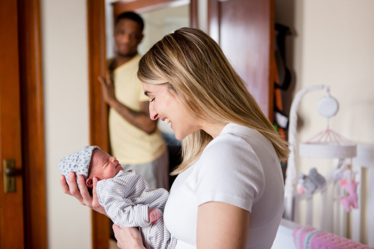 mom smiles at newborn while dad looks on proudly from the doorway
