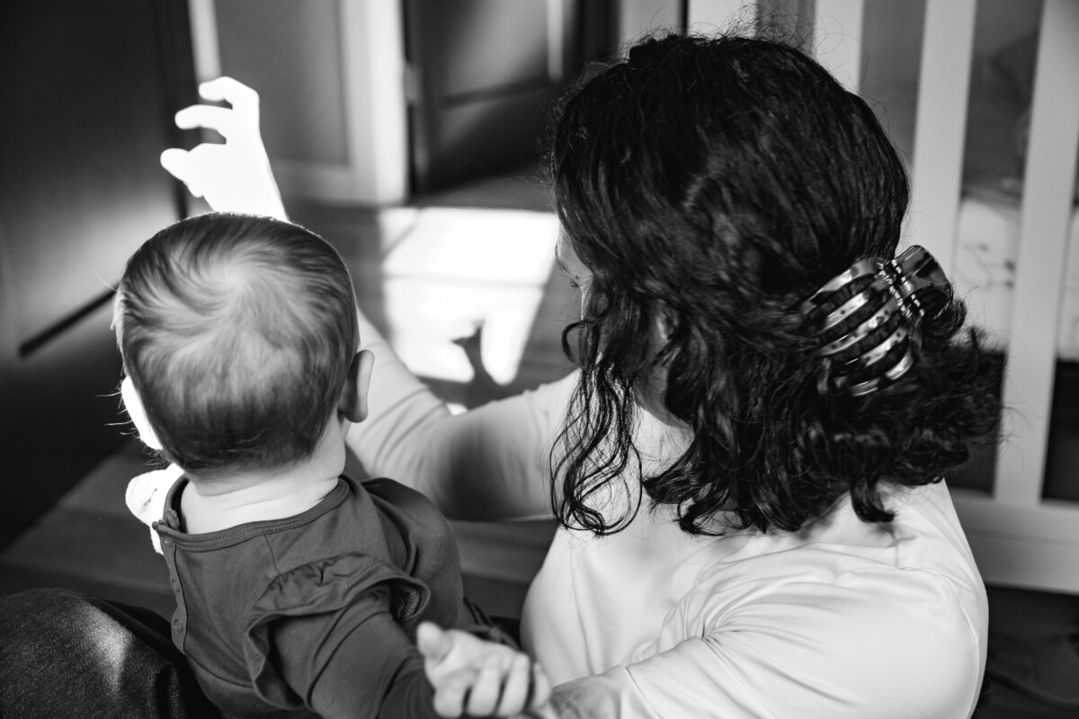Mom making shadow puppets in window light while holding baby during an in-home family photography session