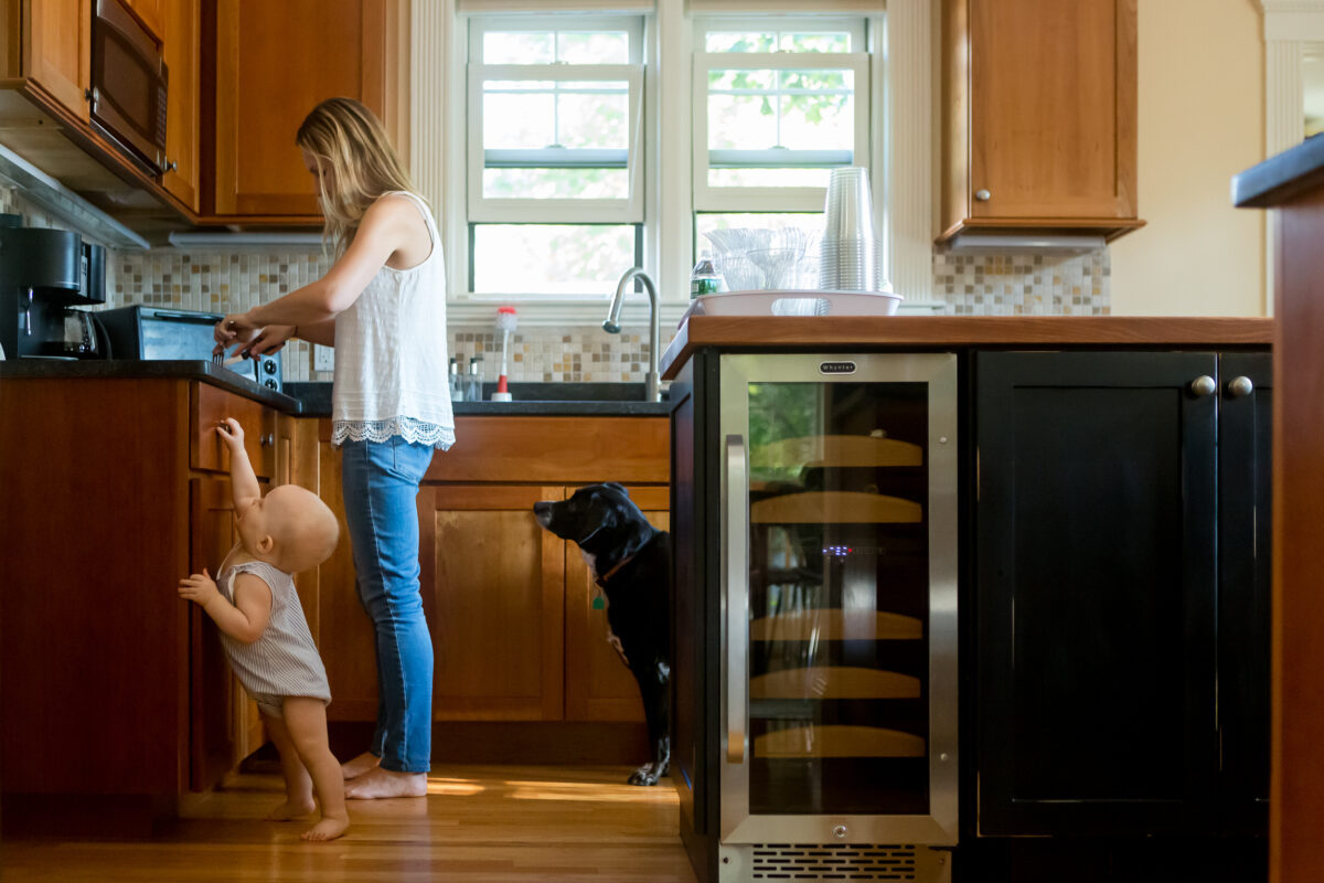baby reaches for the kitchen counter while mom prepares a snack and dog looks on during an in-home family photography session