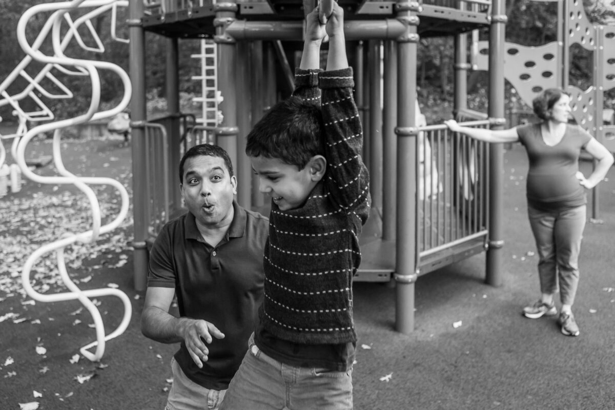 dad and son play on monkey bars with mom in the background