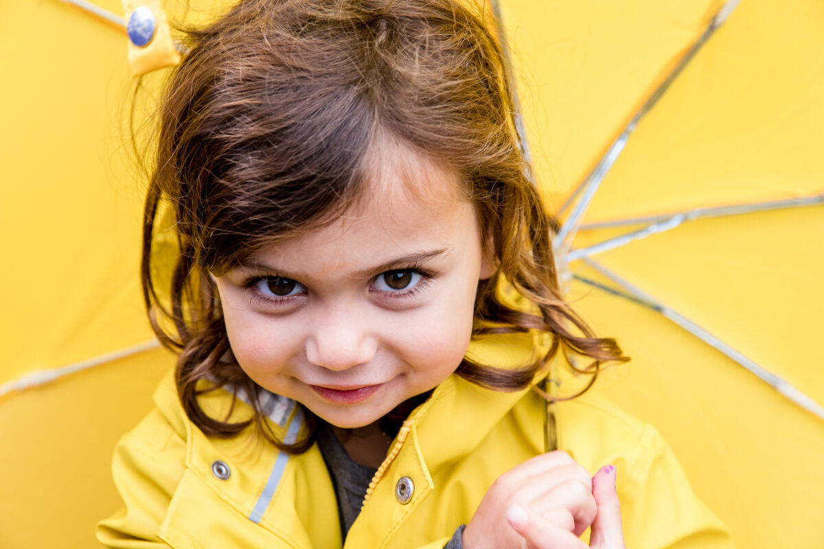 little girl wearing a yellow raincoat under her yellow umbrella