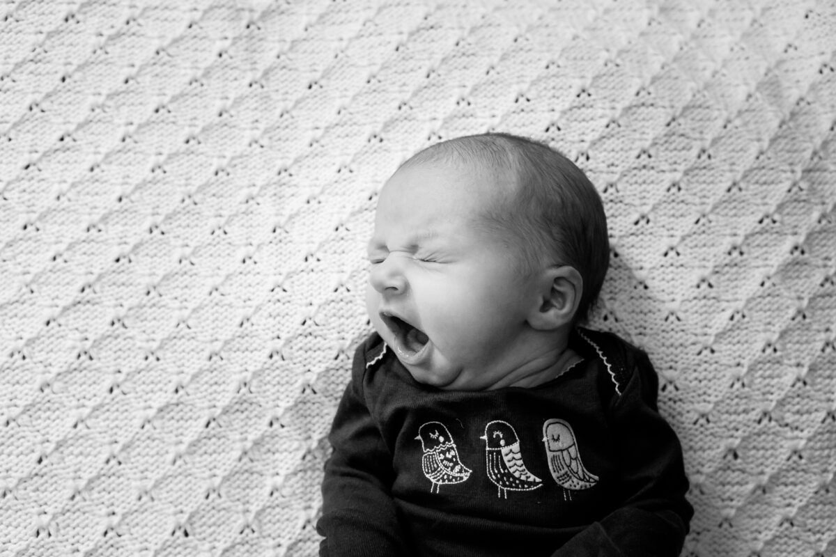 baby yawns while resting on a knitted blanket