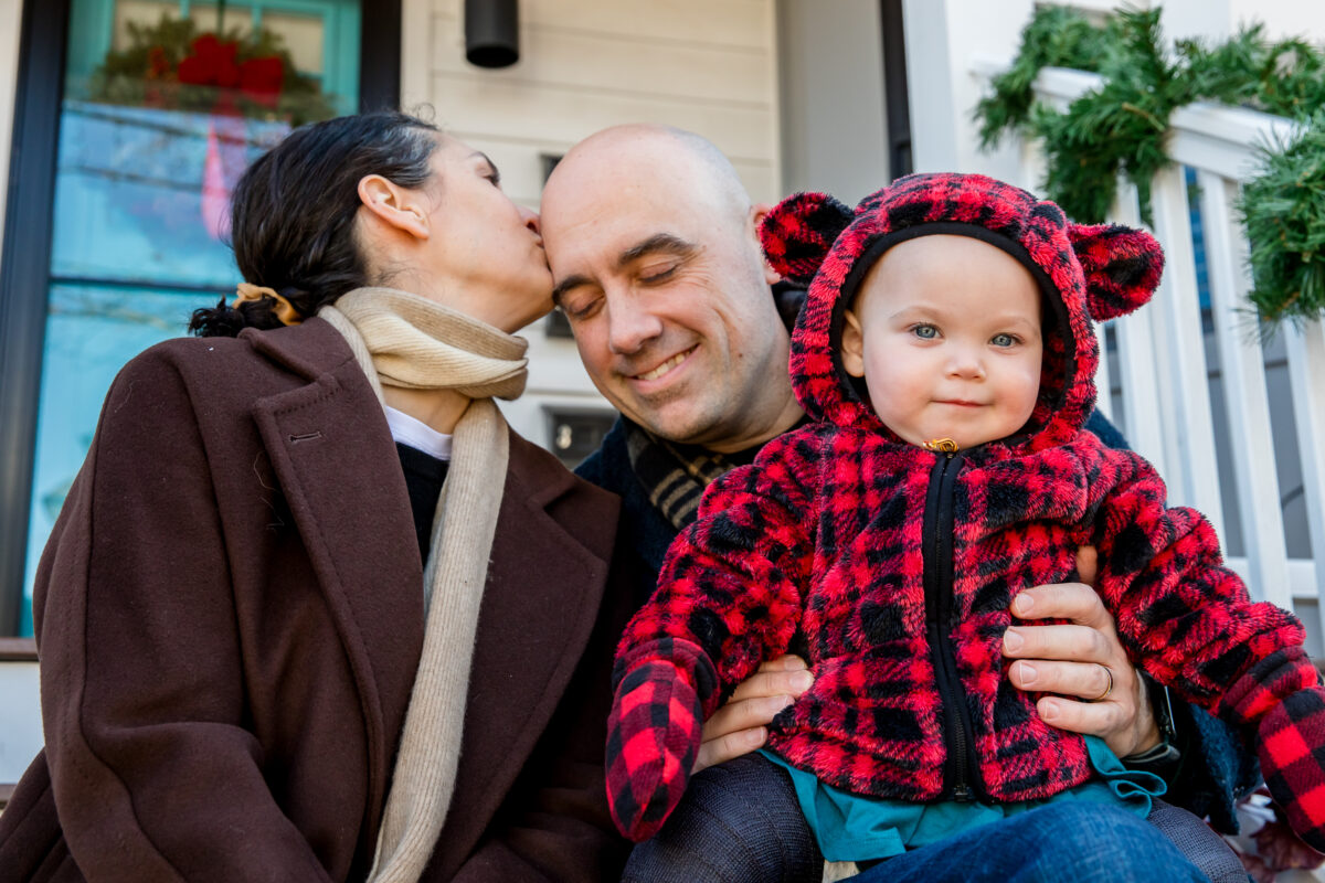 mom kisses dad while he holds baby on their front steps