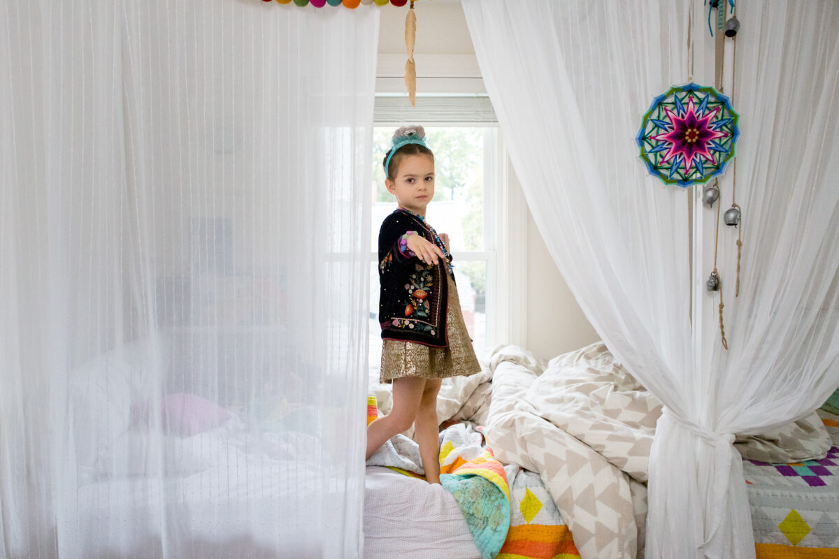 child looks out from the curtains surrounding her bed