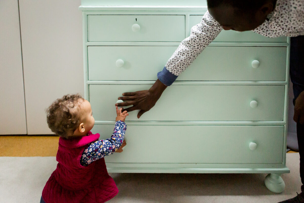 dad and toddler touch hands in front of a mint green dresser