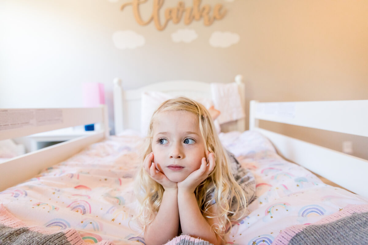 girl rests her chin in her hands on her bed during a family session at home