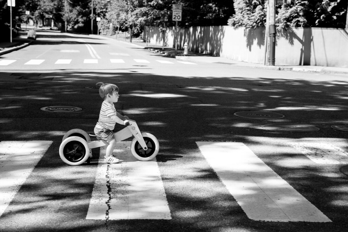 toddler rides his tricycle across a crosswalk in an empty street during a Cambridge family session