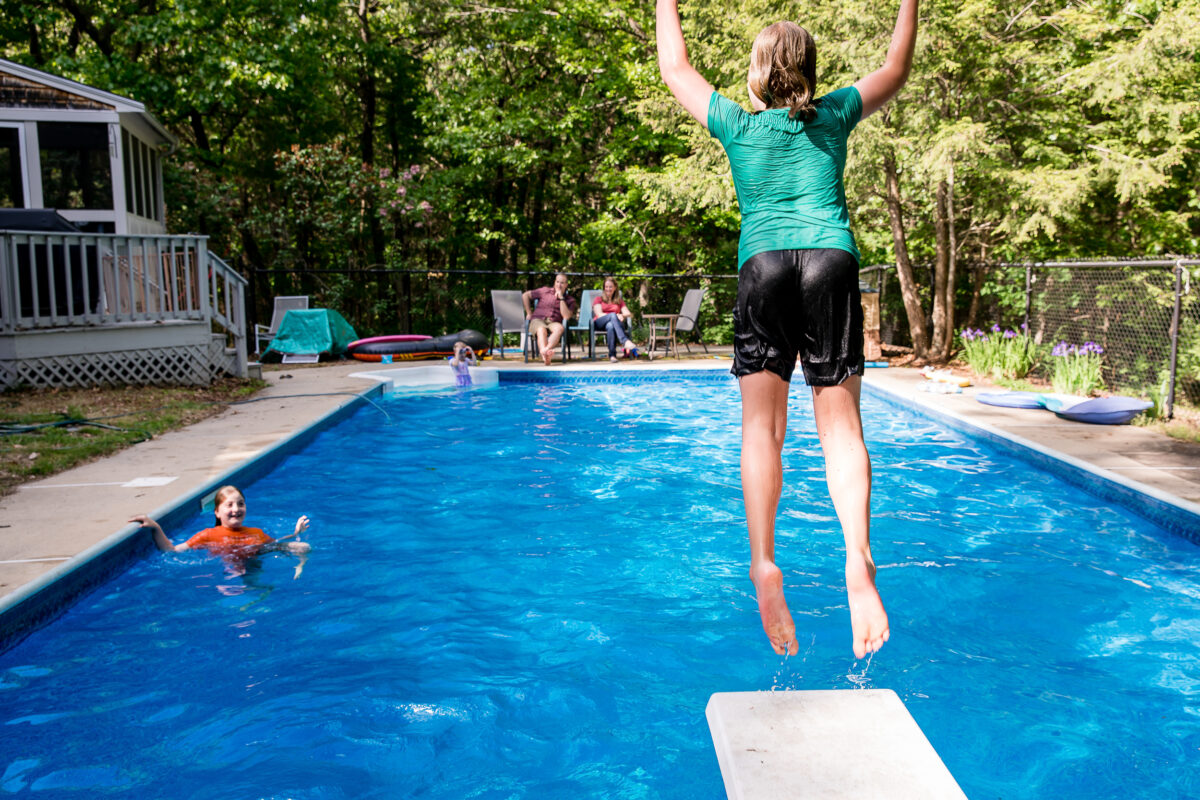 kid jumps into family's pool while parents and siblings look on during an in-home family session