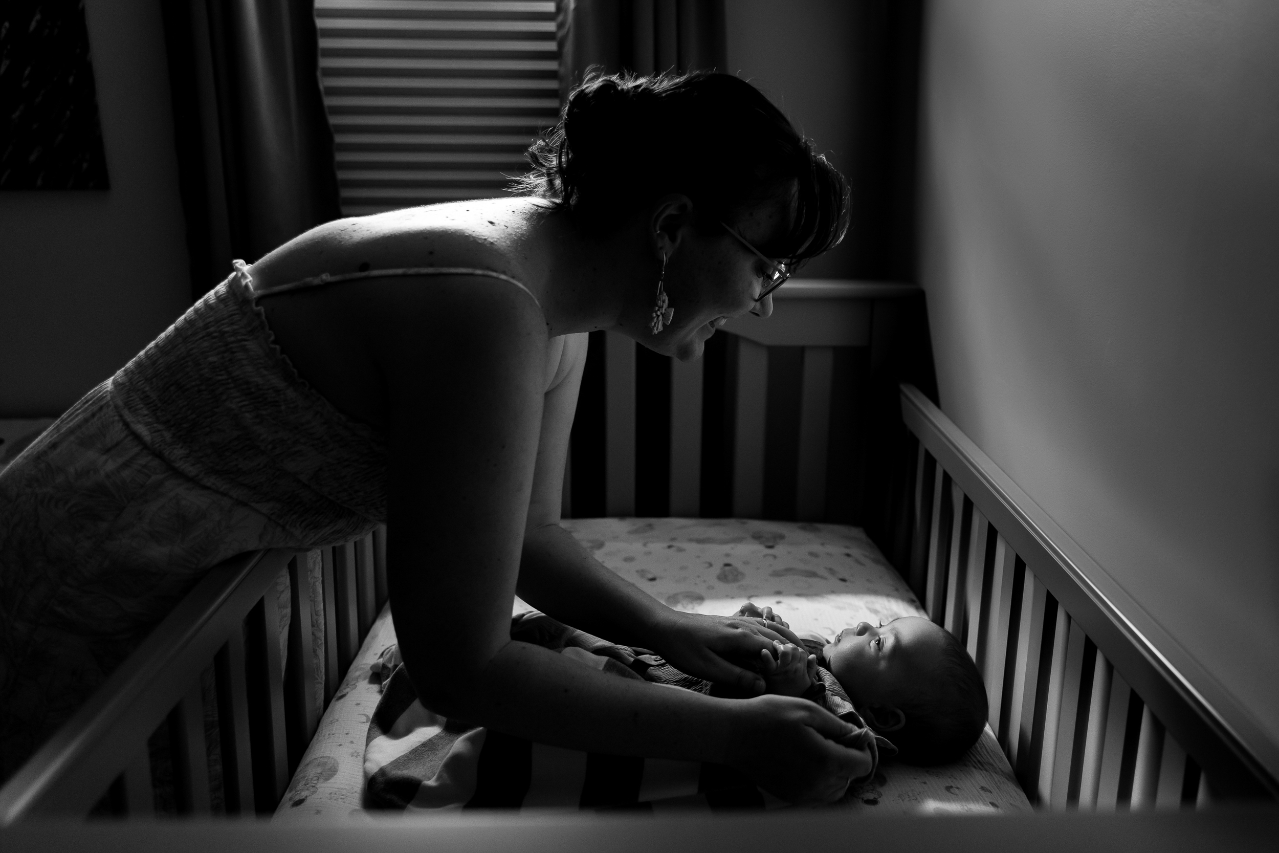 mom gazes upon her baby in crib a darkened room preparing for a nap