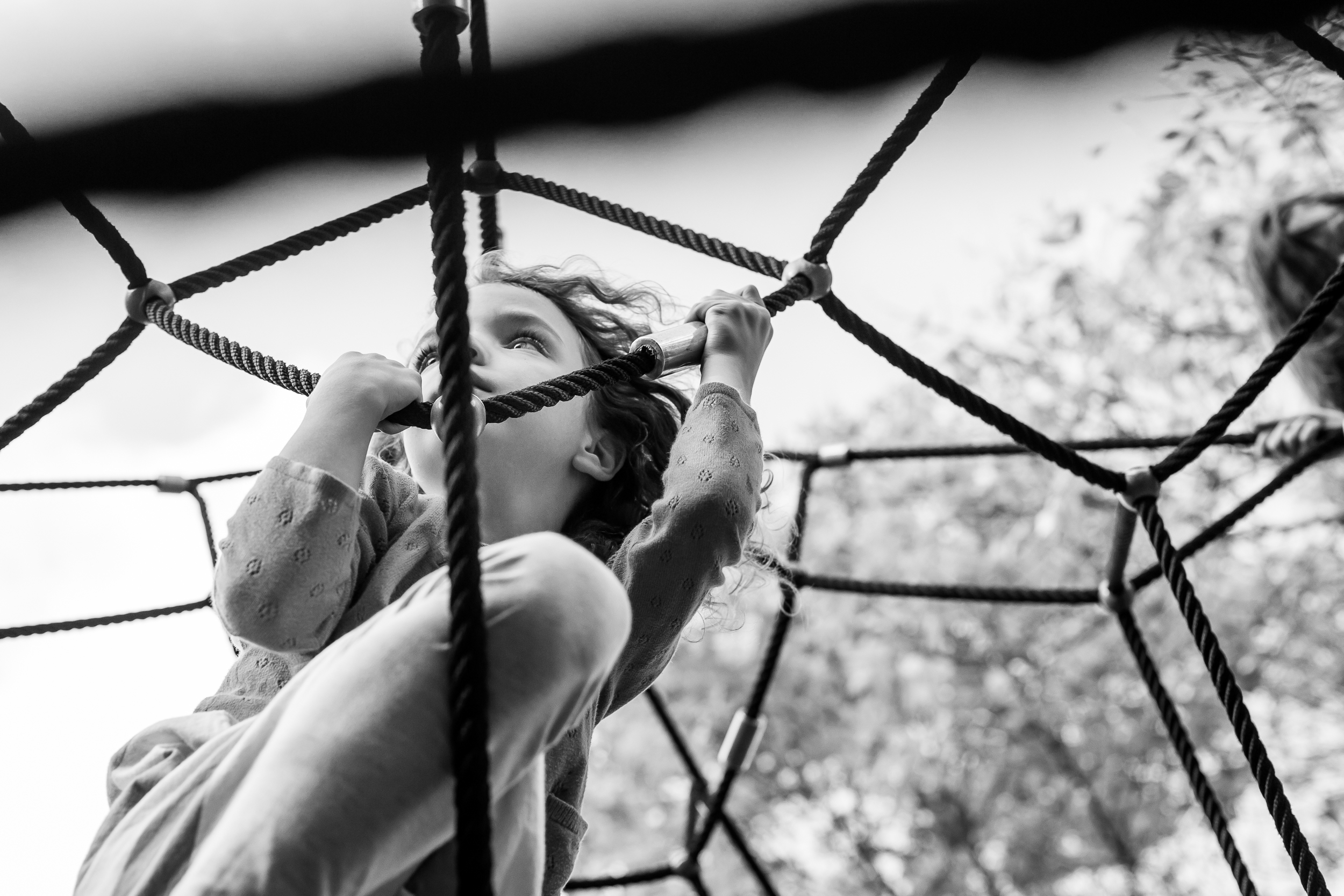 view from below of a girl who has climbed to the top of a rope playground structure during a cambridge family photo session