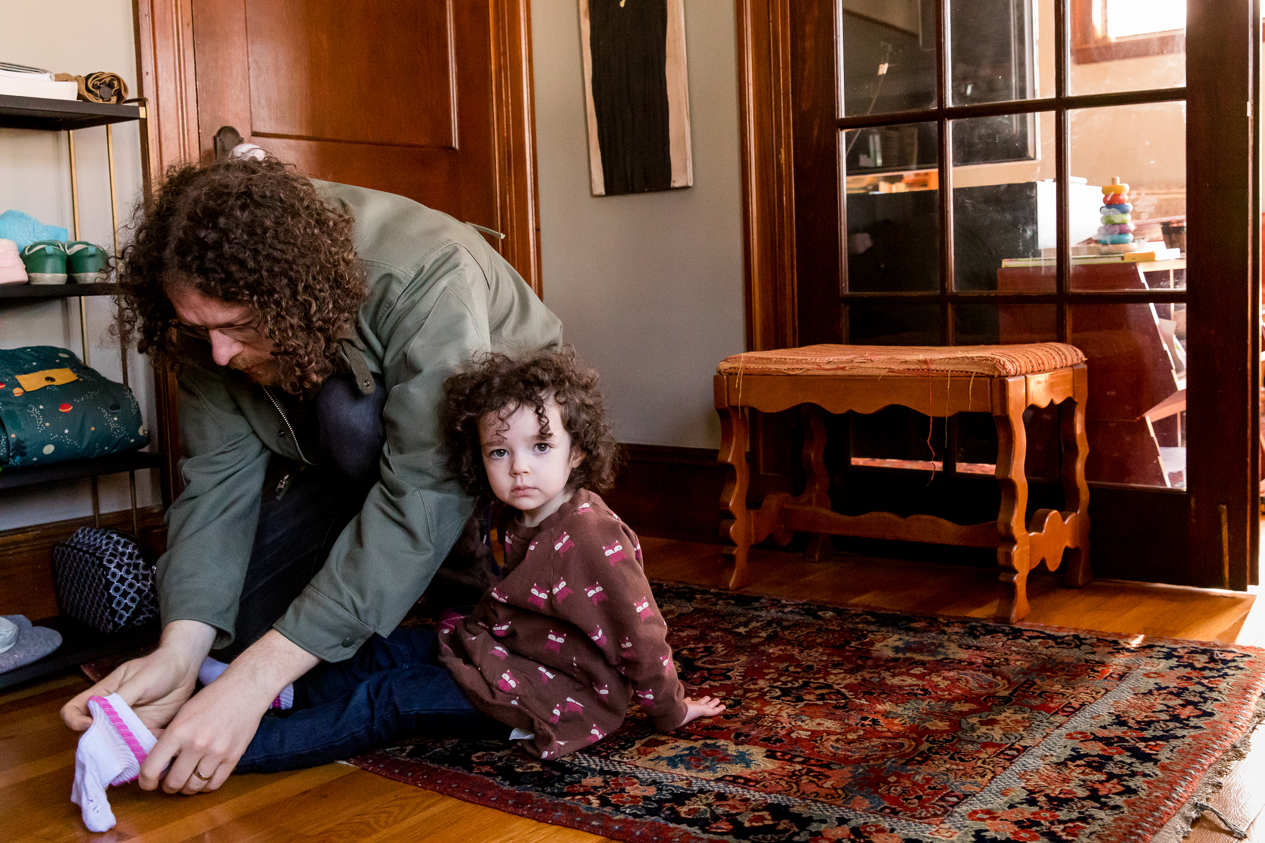 curly haired girl gets help putting on shoes and socks from her curly haired dad