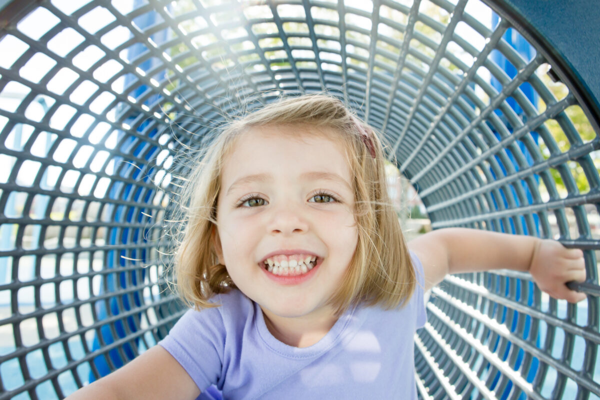 little girl smiles big from inside a metal mesh playground structure