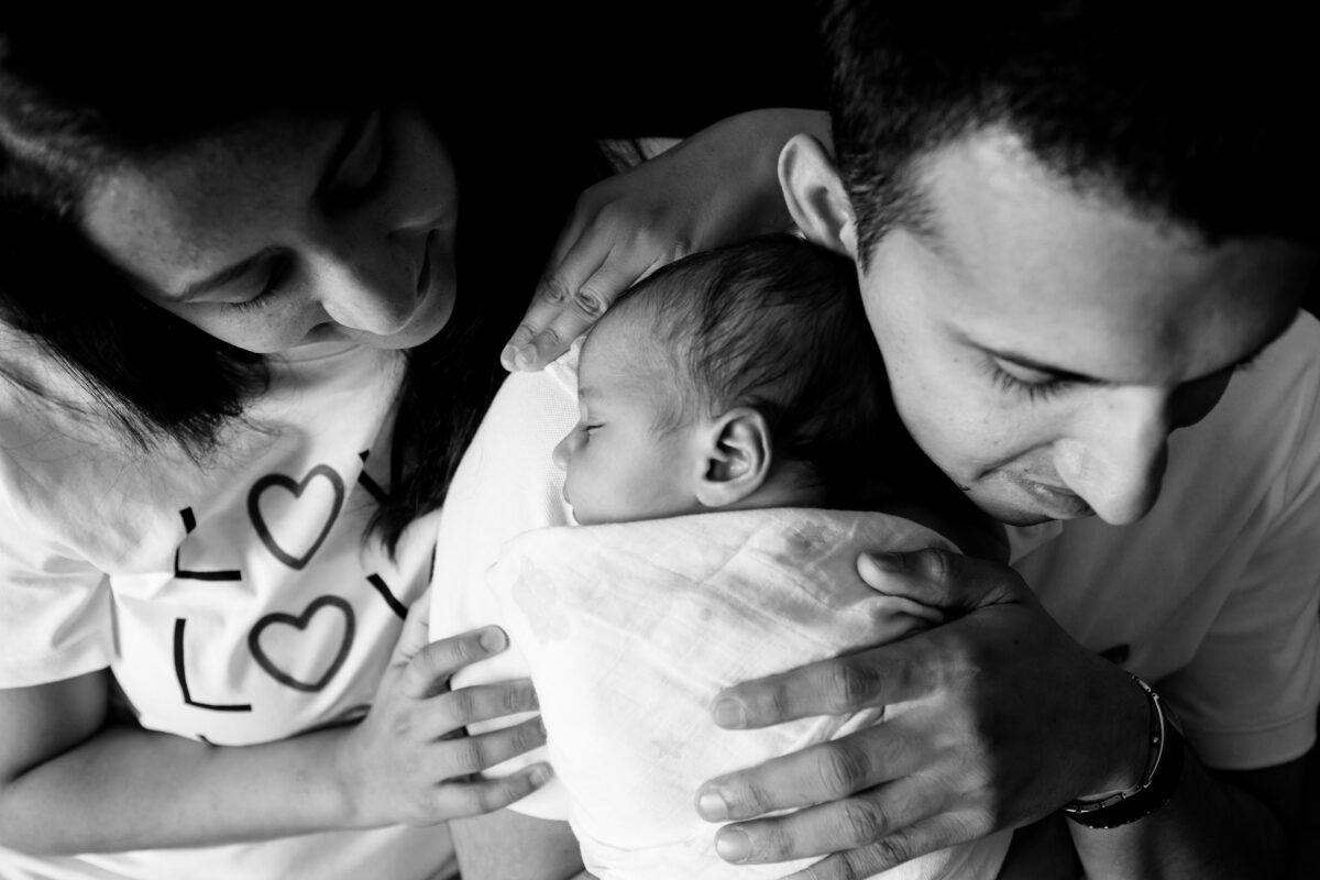 mom and dad hold newborn baby close during a family photography session