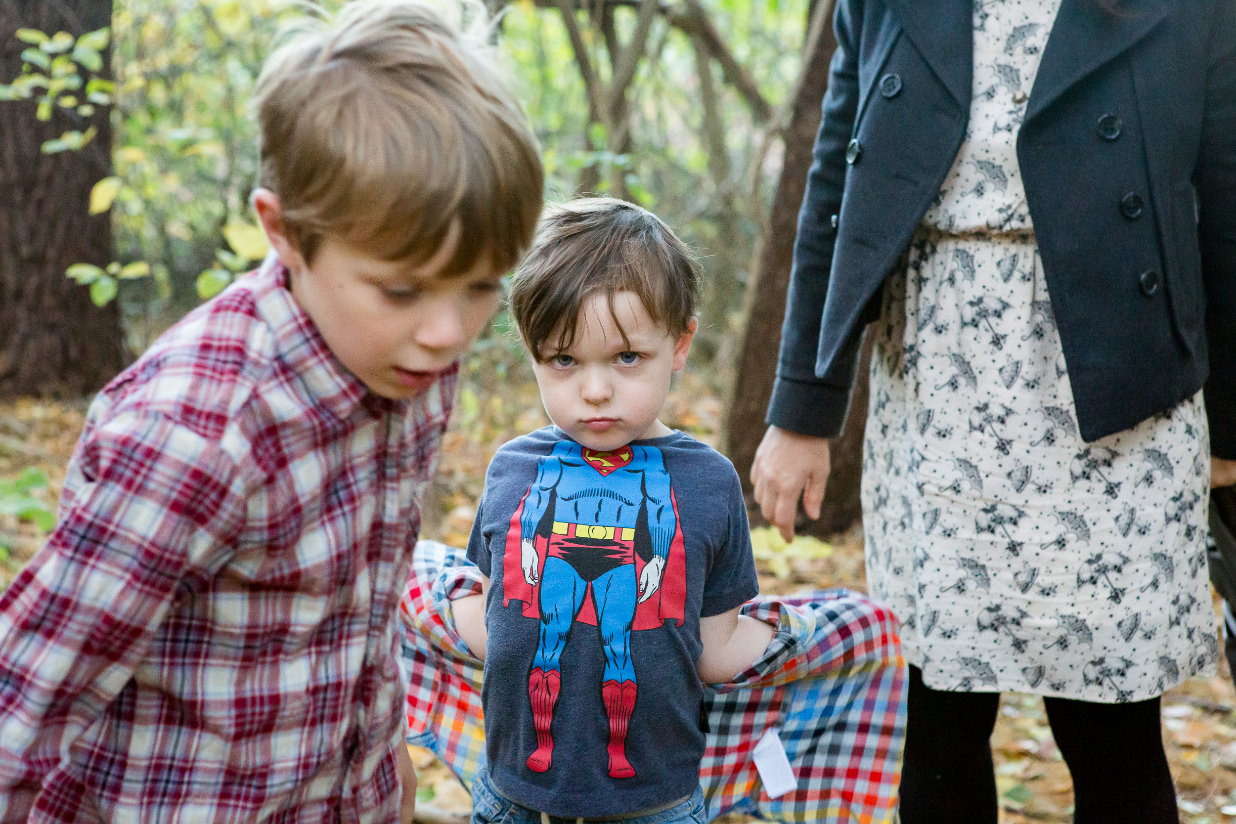 boy with superhero t shirt stares at the camera near his brother and mom during a family photography session; photo by Cambridge Family Photographer Emily Sterne