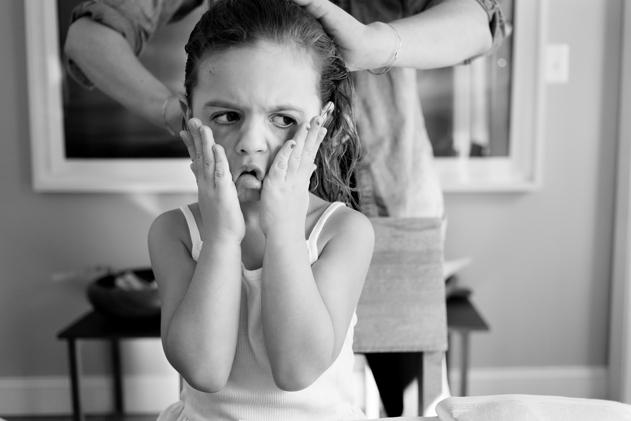 girl having her hair braided is pulling on her face with a skeptical expression