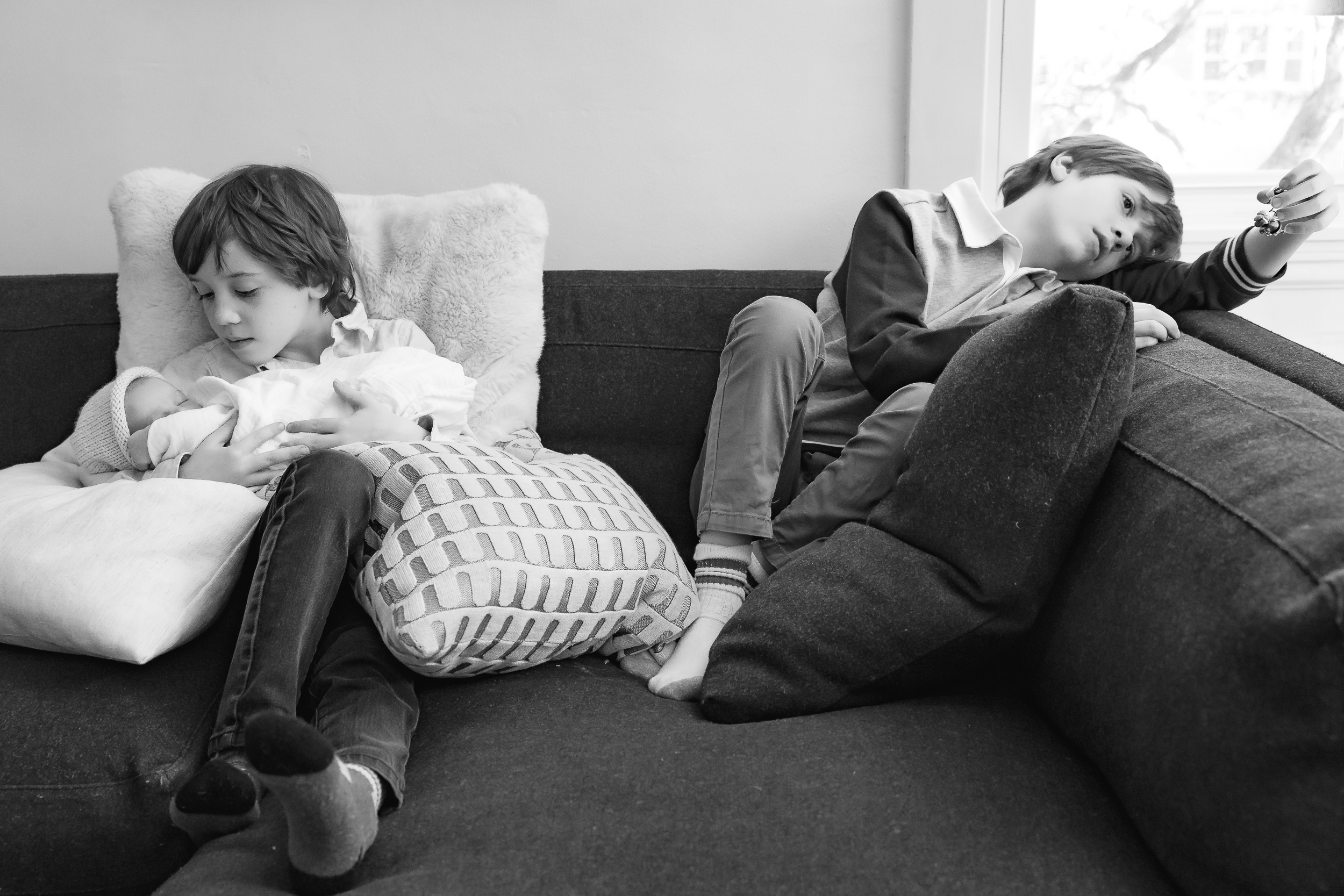 one brother looks bored on the couch while the other one holds baby sister
