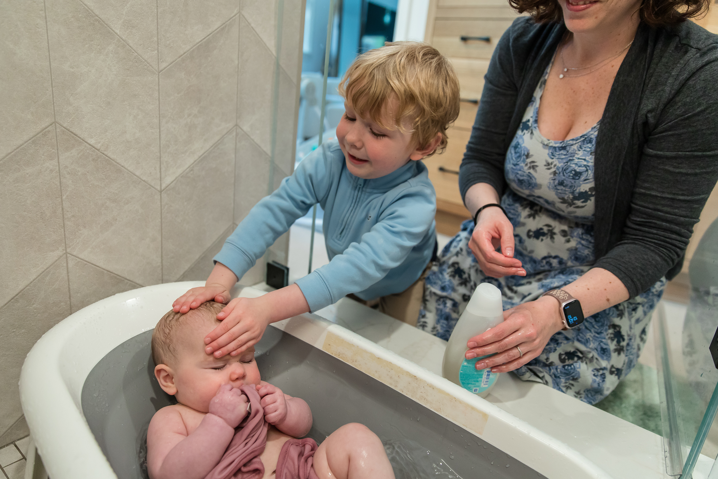 young boy helps shampoo his baby sister during bathtime in a documentary family photography session with emily sterne