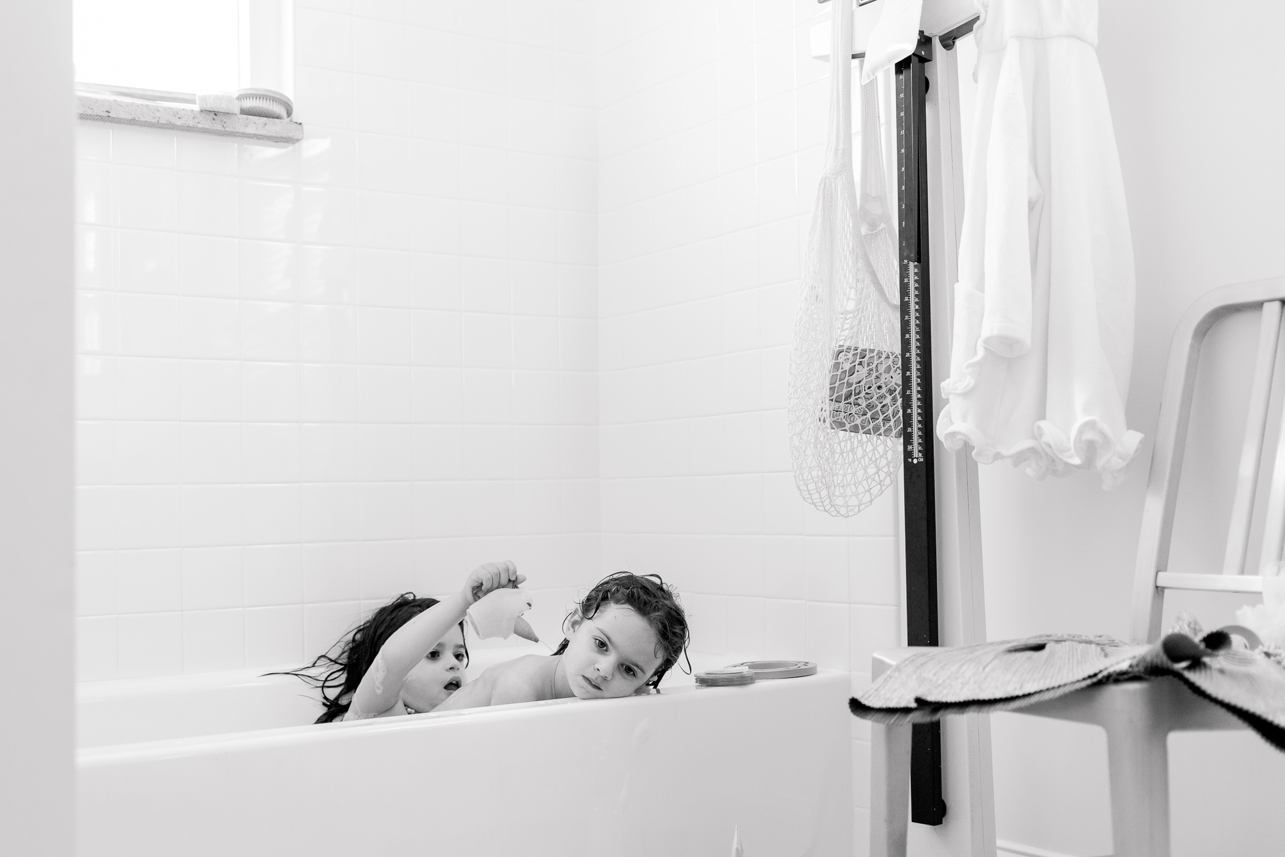 child pours water over her sister in the bath during a documentary family photography session with emily sterne